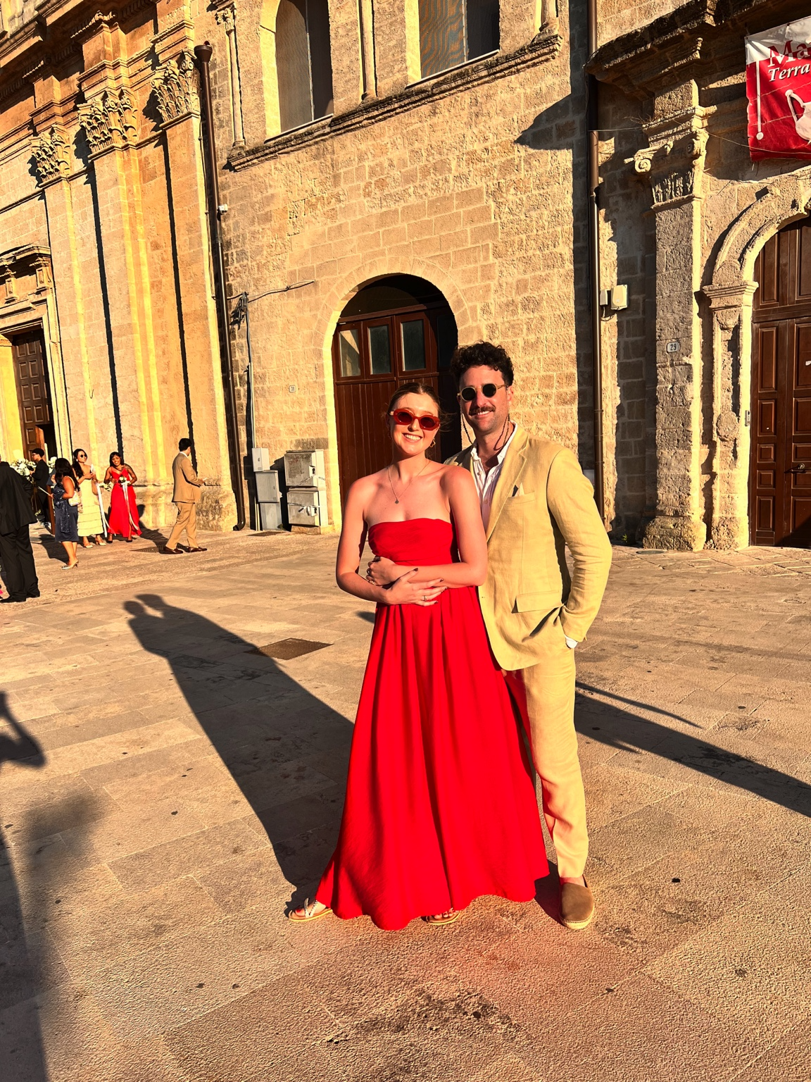 Chloe in a red dress and Gal in a beige suit at sunset